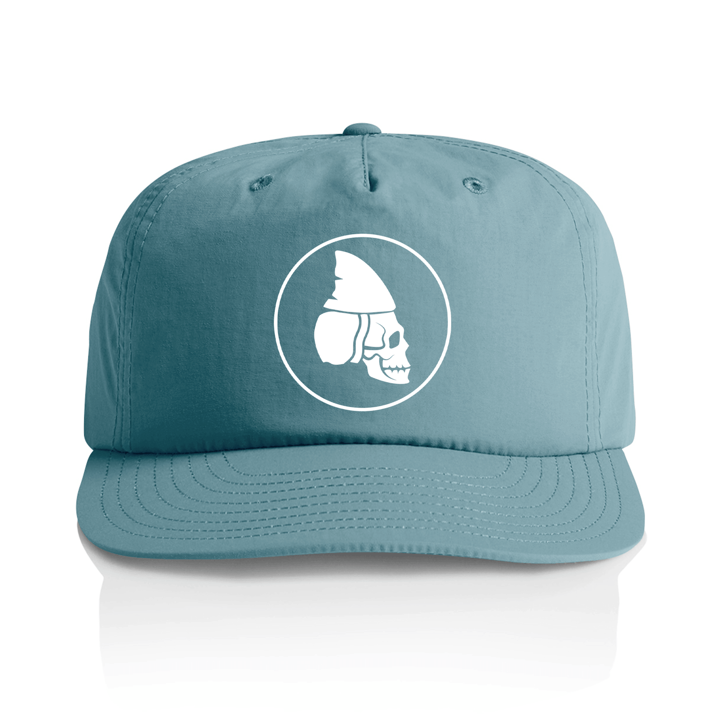 A slate blue snapback cap with a white circular graphic on the front depicting a skull wearing a helmet, shown against a plain white background with a soft reflection below.
