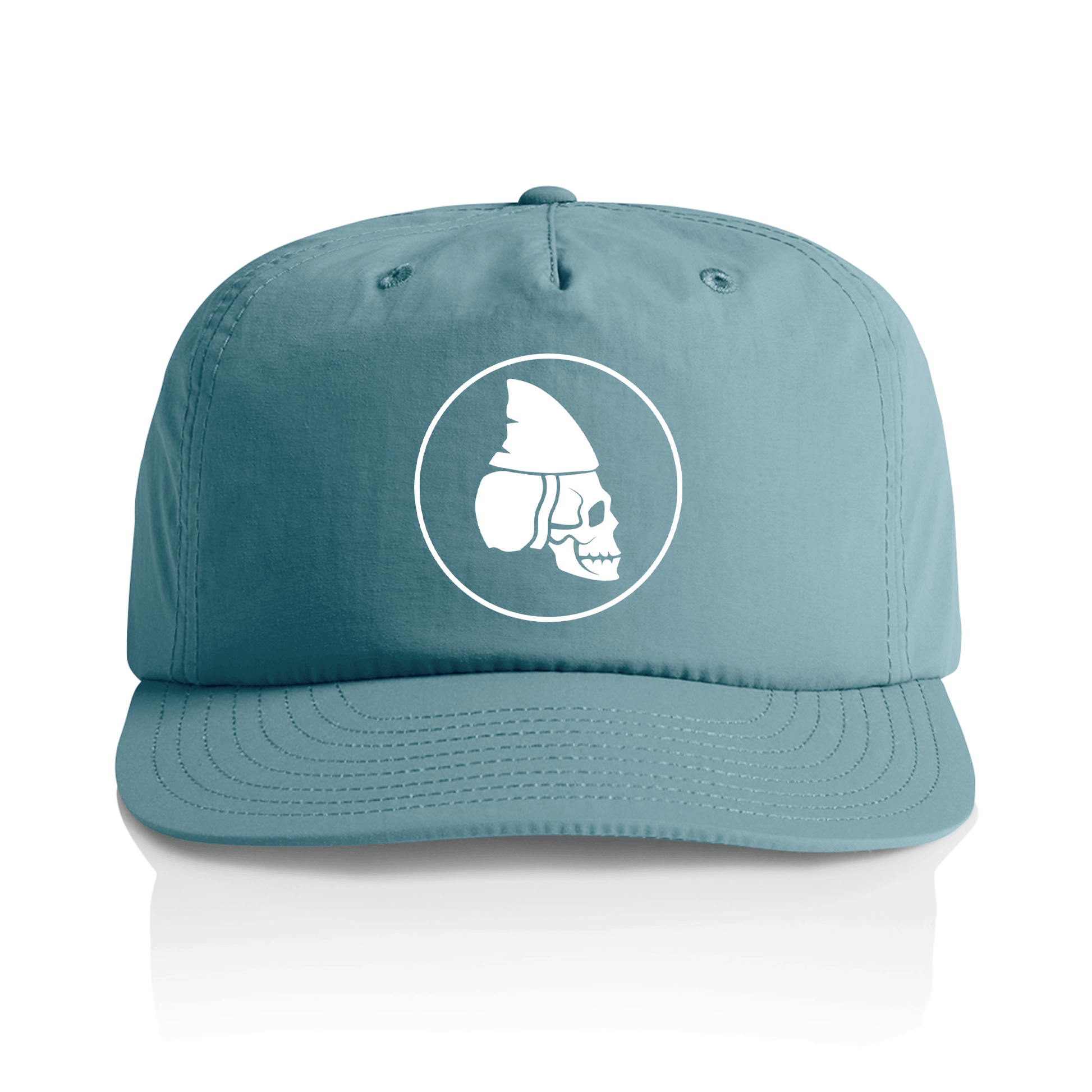 A slate blue snapback cap with a white circular graphic on the front depicting a skull wearing a helmet, shown against a plain white background with a soft reflection below.